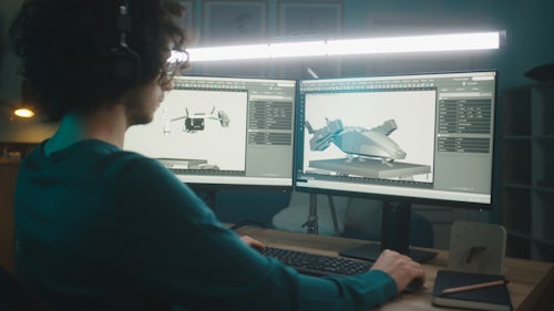 An aerospace engineer is shown sitting at a desk working on designs on a computer